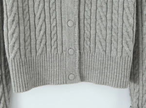 Detailed view of light gray cable-knit cardigan with fabric buttons and ribbed hem