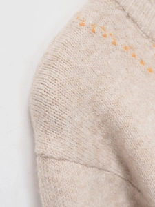 Close-up of beige chunky knit sweater featuring orange geometric embroidery and stitching