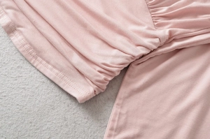 Detail of delicate ruched stitching and pastel pink knit fabric on women's blouse sleeve