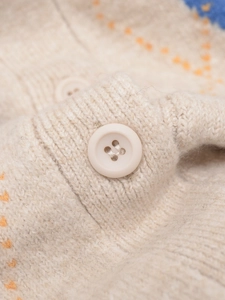 Close-up of beige wool knit texture with orange diamond patterns and a matte button