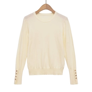 Detailed view of cream knit sweater sleeve featuring elegant gold buttons on ribbed cuffs