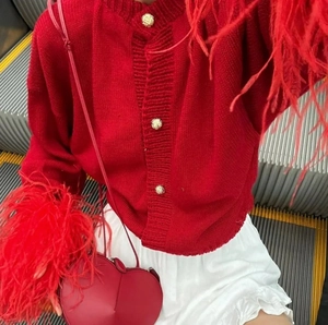Detail of red knit cardigan featuring fluffy feather cuffs and golden textured buttons