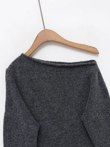 Détail de la texture du pull en tricot gris foncé et du col bateau sur un cintre