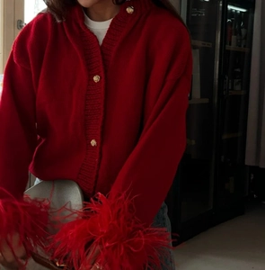 Close-up of red knit cardigan featuring faux feather cuffs and elegant gold buttons