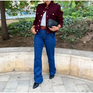 Détail d'une veste courte bordeaux à boutons dorés et d'un jean taille haute ajusté