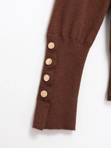 Detailed close-up of brown knit sweater cuff featuring elegant golden decorative buttons