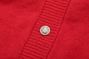 Close-up of red ribbed knit cardigan featuring a vintage silver crest metal button