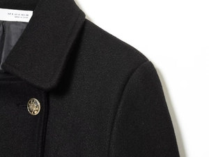 Dettaglio del cappotto di lana nero con bottoni dorati a stemma ed etichetta della taglia