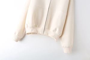 Detail of ribbed hem and metallic zipper on a beige bomber jacket hoodie