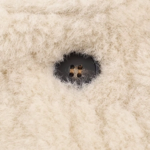 Macro shot of a dark four-hole button on high-quality off-white faux fur jacket fabric