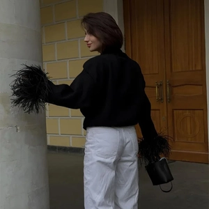 Close-up of elegant black knit cardigan featuring luxurious faux feather trim on the cuffs