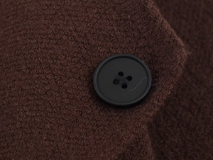 Macro detail of high-quality dark brown knit fabric with a black matte button closure