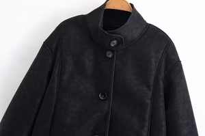 Détail de la texture mate noire sur une veste minimaliste à col montant et boutons simples