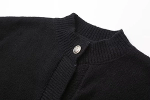 Macro detail of ribbed crew neck on black cardigan with embossed silver metal button