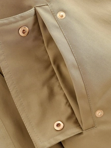 Detalle en macro de la chaqueta acolchada caqui con botones de presión dorados en el bolsillo