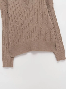 Detail of light brown cable-knit V-neck sweater with ribbed cuffs and soft texture