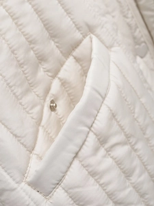 Macro detail of ivory quilted jacket showing diamond stitching and metal snap pocket