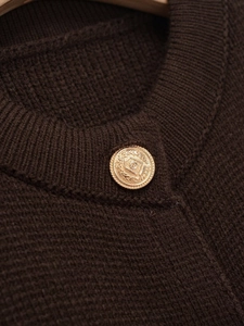 Close-up of dark brown knit cardigan collar with vintage gold relief crest button