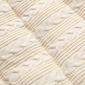 Macro shot of ivory knit fabric featuring thick classic cable stitch textures and patterns