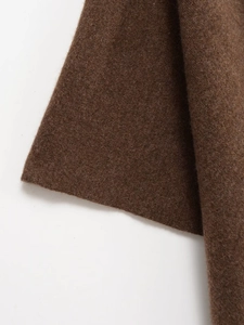 Gros plan du tissu du poncho en maille marron montrant sa surface texturée en laine