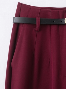 Détail du pantalon bordeaux avec plis à la taille et ceinture en cuir noir avec boucle