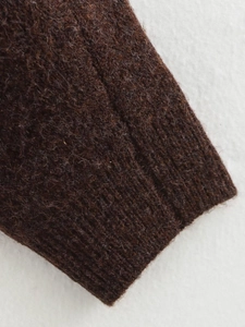 Détail macro du poignet d'un pull en maille marron foncé avec texture côtelée et tissu doux