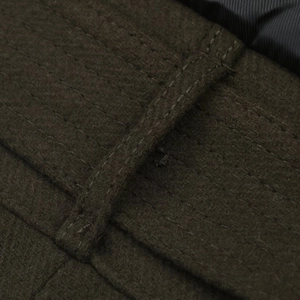 Detailed close-up of dark olive wool jacket with reinforced belt loop and heavy stitching