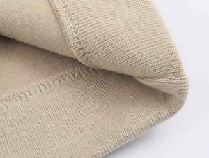 Macro shot of beige ribbed knit fabric showing high-quality overlock stitching detail