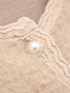Detail of faux mink knit cardigan with pearl buttons and wavy edge trim in beige