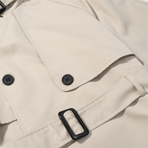 Detail shot of the beige trench coat pocket with black button and waist belt strap