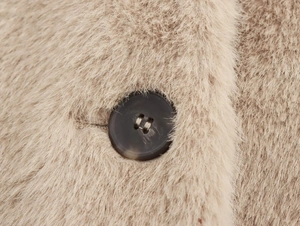 Détail de la texture en fausse fourrure camel douce et bouton en résine marron sur la veste