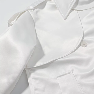 Close-up of white satin trench coat featuring shoulder straps and oversized lapels