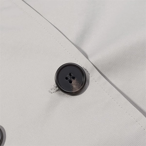 Detail of light gray twill fabric and premium black button on a double-breasted trench coat