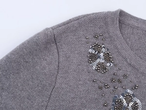 Close-up of elegant beaded flower pattern and soft knit texture on grey round-neck cardigan