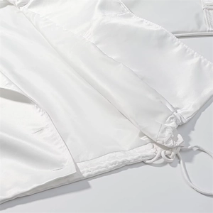 Detail of white cropped trench coat featuring drawstring hem and glossy fabric texture