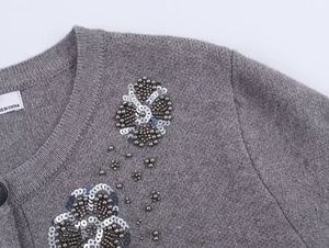 Macro detail of gray knit cardigan featuring intricate silver flower beadwork and sequins