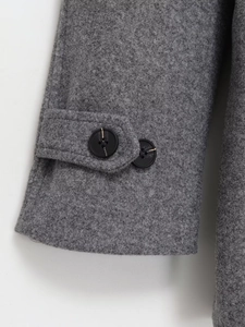 Détail de la manche d'un manteau en laine grise avec patte décorative et boutons noirs