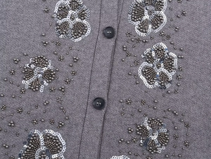 Detail of grey knit cardigan featuring black buttons and silver floral sequin beadwork