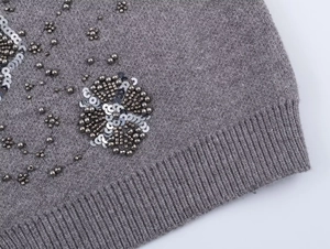 Detail of grey knit cardigan showing intricate 3D floral beadwork and silver sequins