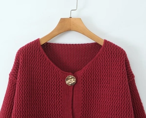 Dettaglio del cardigan rosso a maglia traforata con elegante bottone dorato a sbalzo