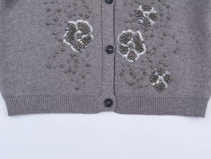 Detail of gray knit cardigan featuring handmade 3D floral beadwork and silver sequins