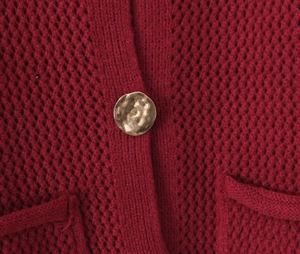Dettaglio del cardigan rosso vino in maglia traforata con bottone dorato martellato
