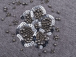 Macro shot of intricate silver beadwork and floral sequins on dark grey knit cardigan