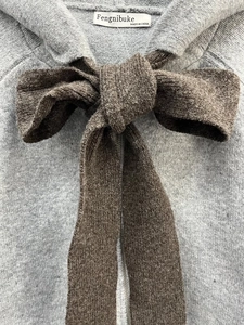 Close-up of grey knitted hoodie texture with large brown decorative bow and inner collar label