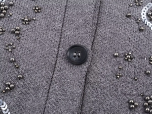 Close-up of grey knit cardigan featuring black buttons and beaded sequin embellishments