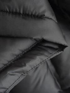 Nahaufnahme der schwarzen Steppweste mit Kapuze, horizontaler Steppung und Nylon-Oberfläche
