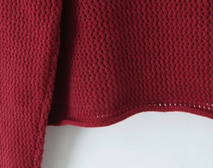 Dettaglio macro del cardigan bordeaux con trama a nido d'ape e bordo inferiore a rullo
