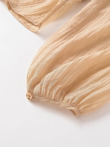 Détail de la manche d'une chemise beige plissée transparente avec bouton doré
