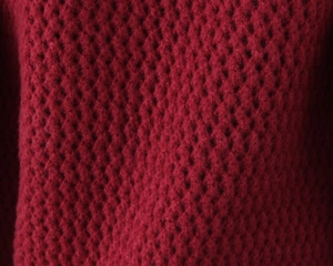 Dettaglio del cardigan rosso in maglia con trama a nido d'ape e motivo a nido d'ape