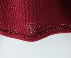 Dettaglio macro del cardigan in maglia rosso scuro con motivi pointelle e bordo a coste